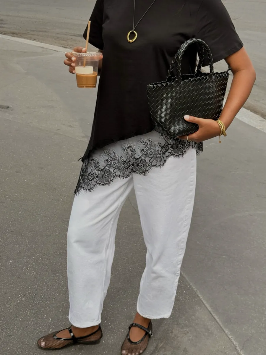 Close-up of a black lace-trim top, white trousers, black woven bag and sandals
