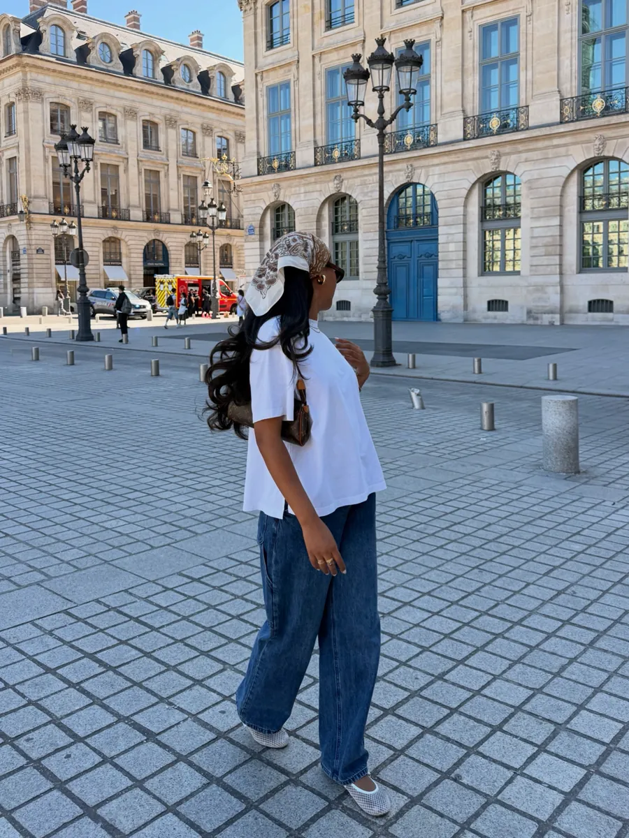 Mia in Place Vendôme in a white shirt, baggy jeans and a bandana, with a backpack