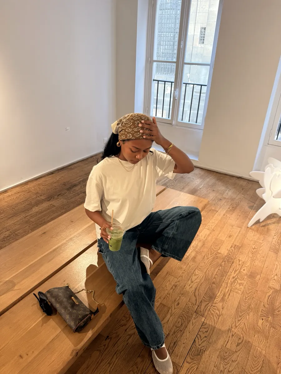 Mia sitting on a wooden step in a cream tee, jeans and bandana
