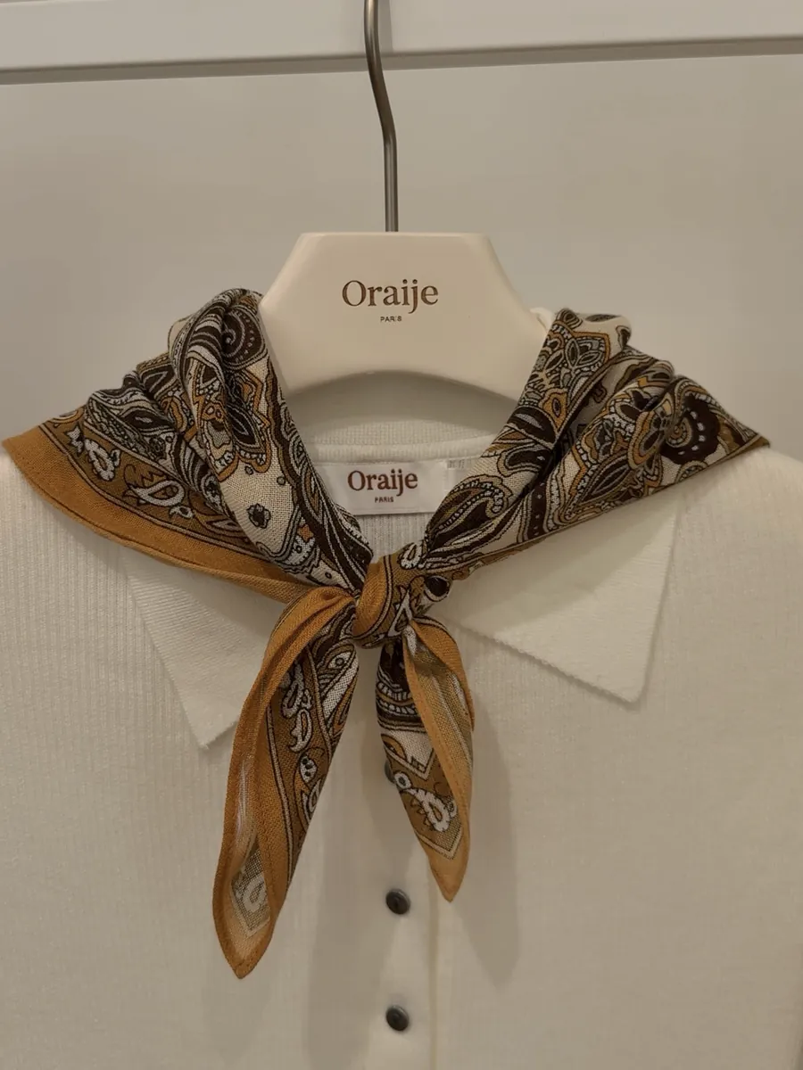 Oraije cream knit cardigan on a hanger with a paisley silk scarf tied at the collar