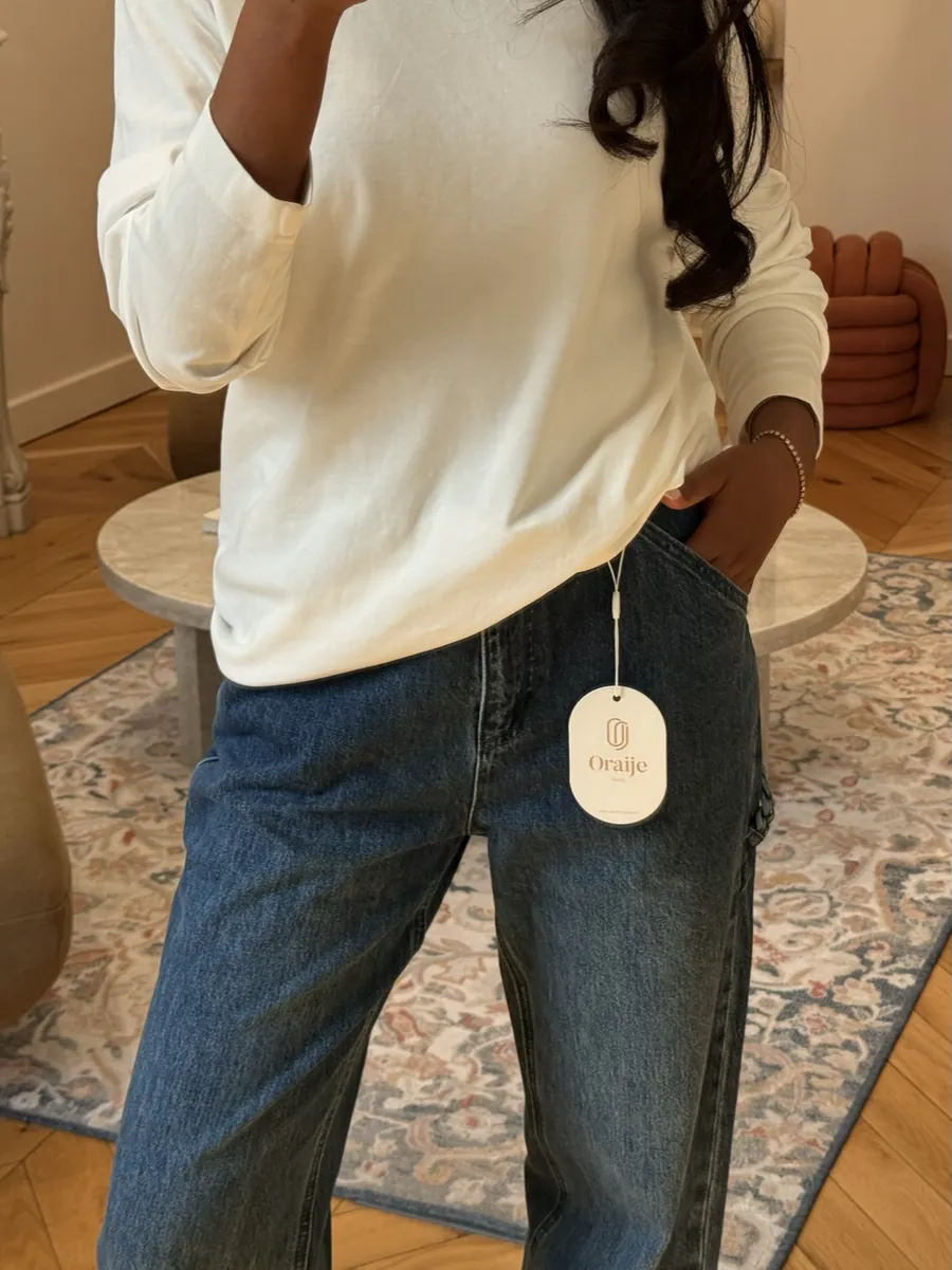 Mia in a cream sweater and straight-leg jeans with an Oraije tag